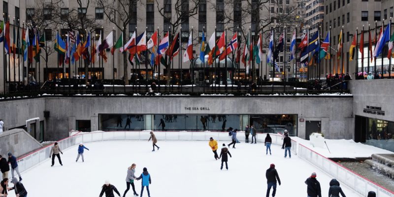 people ice skating on field surrounded by high-rise buildings